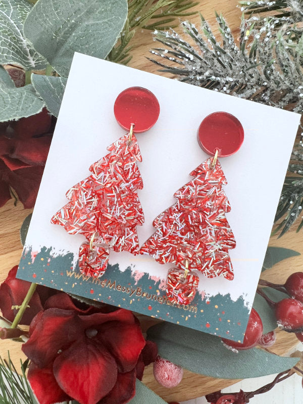 Red Christmas tree earrings on a decorative card with greenery and berries in the background