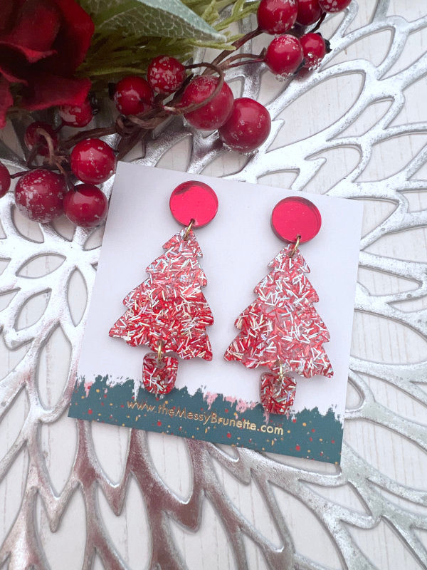Red and white Christmas tree earrings on a decorative card with berries and branches.