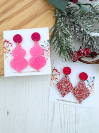 Two pairs of handmade dangle earrings displayed on white cards. One pair features chunky, glittery hot pink gourd-shaped drops with solid magenta circular studs.