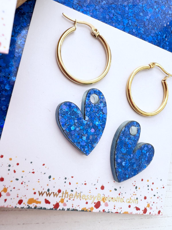 Blue heart-shaped earrings with gold hoops on a colorful card.