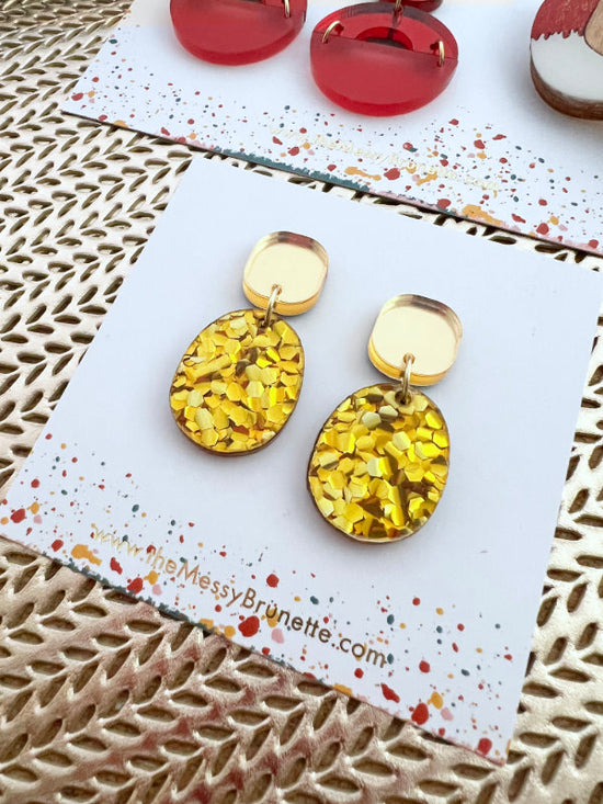Gold and yellow earrings on a branded card with red earrings in the background.