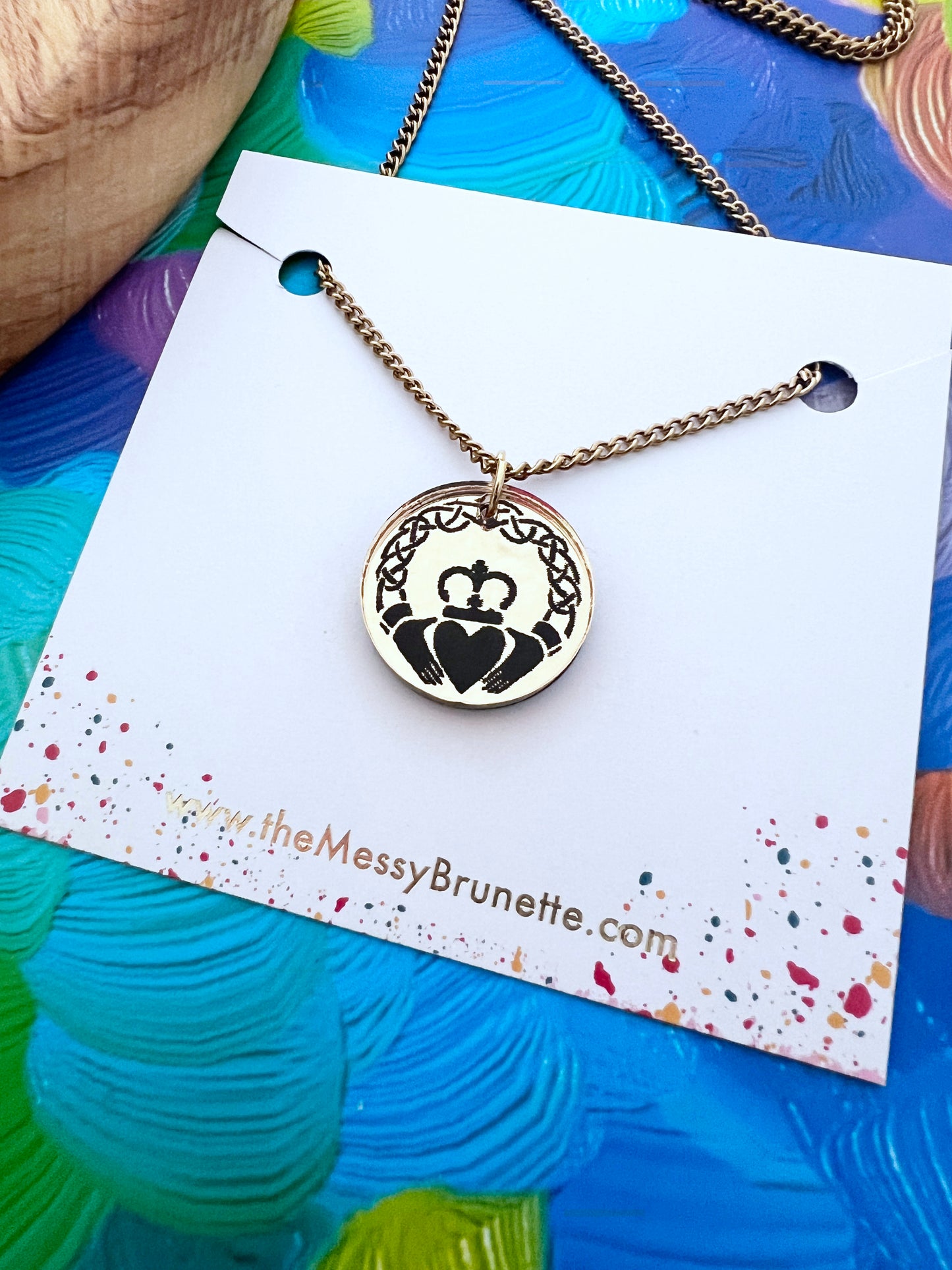 Necklace with a claddagh pendant on a branded card against a colorful background