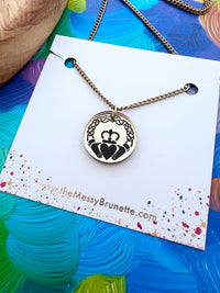 Necklace with a claddagh pendant on a branded card against a colorful background