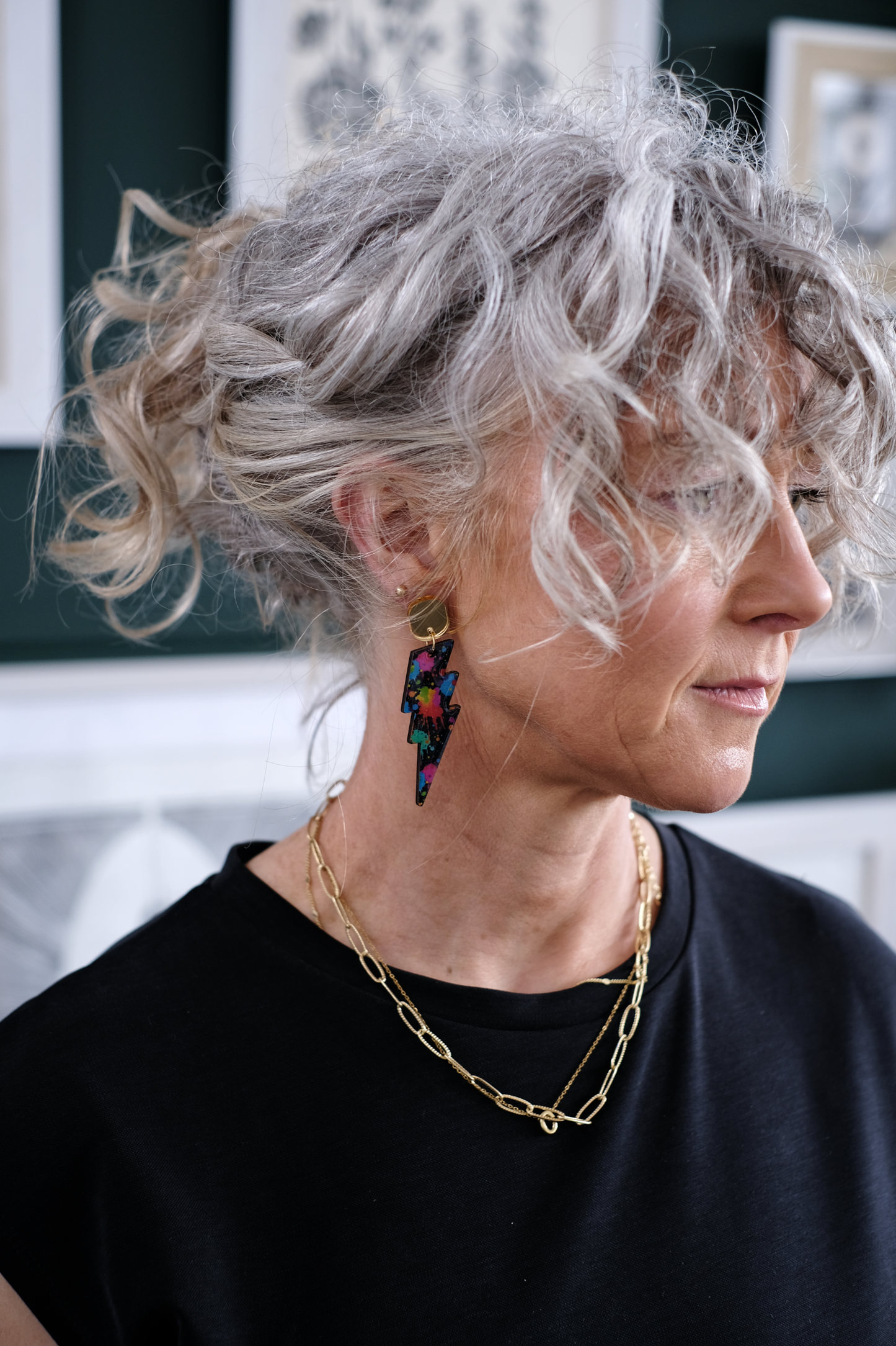 Woman with gray hair wearing colourful bolt earrings and a black top.