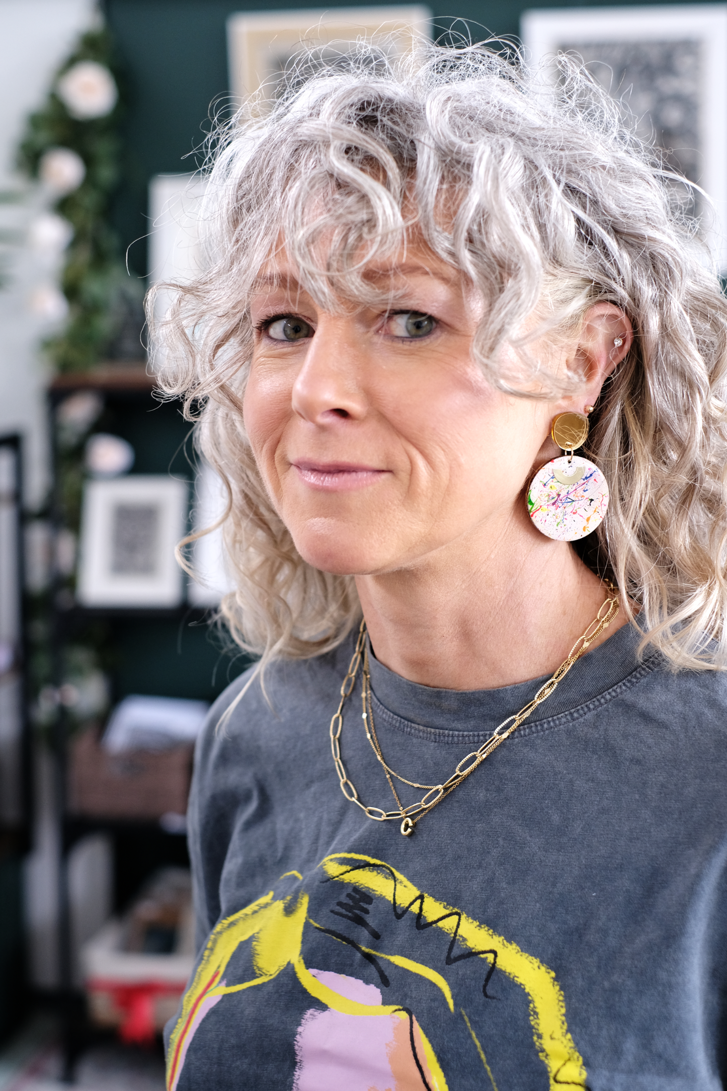 Person with curly hair wearing big paint splatter round wood cirlces earrings