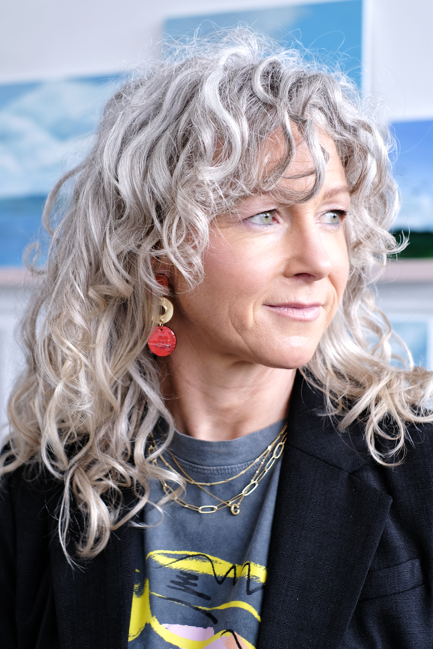 Woman with curly gray hair wearing a orange and gold earring drops