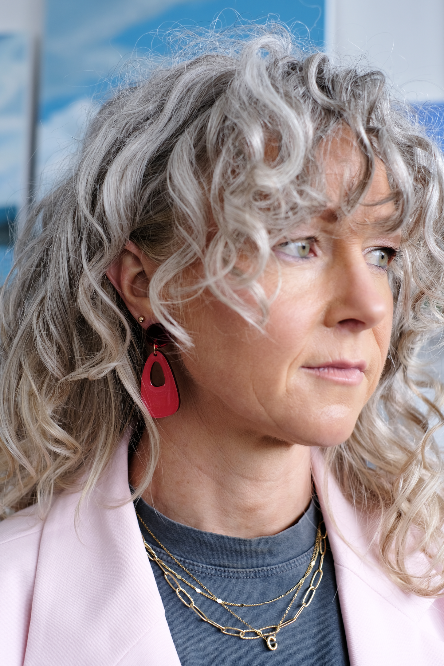 Woman with curly gray hair wearing red hand painted wood earrings and a pink coat.