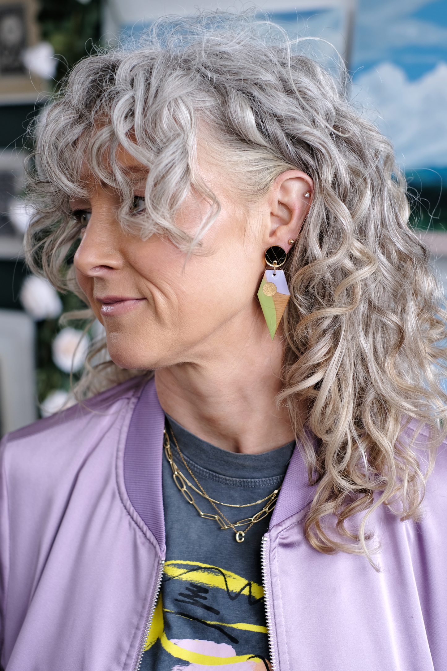 Woman with curly gray hair wearing a purple jacket and geometric wood earrings