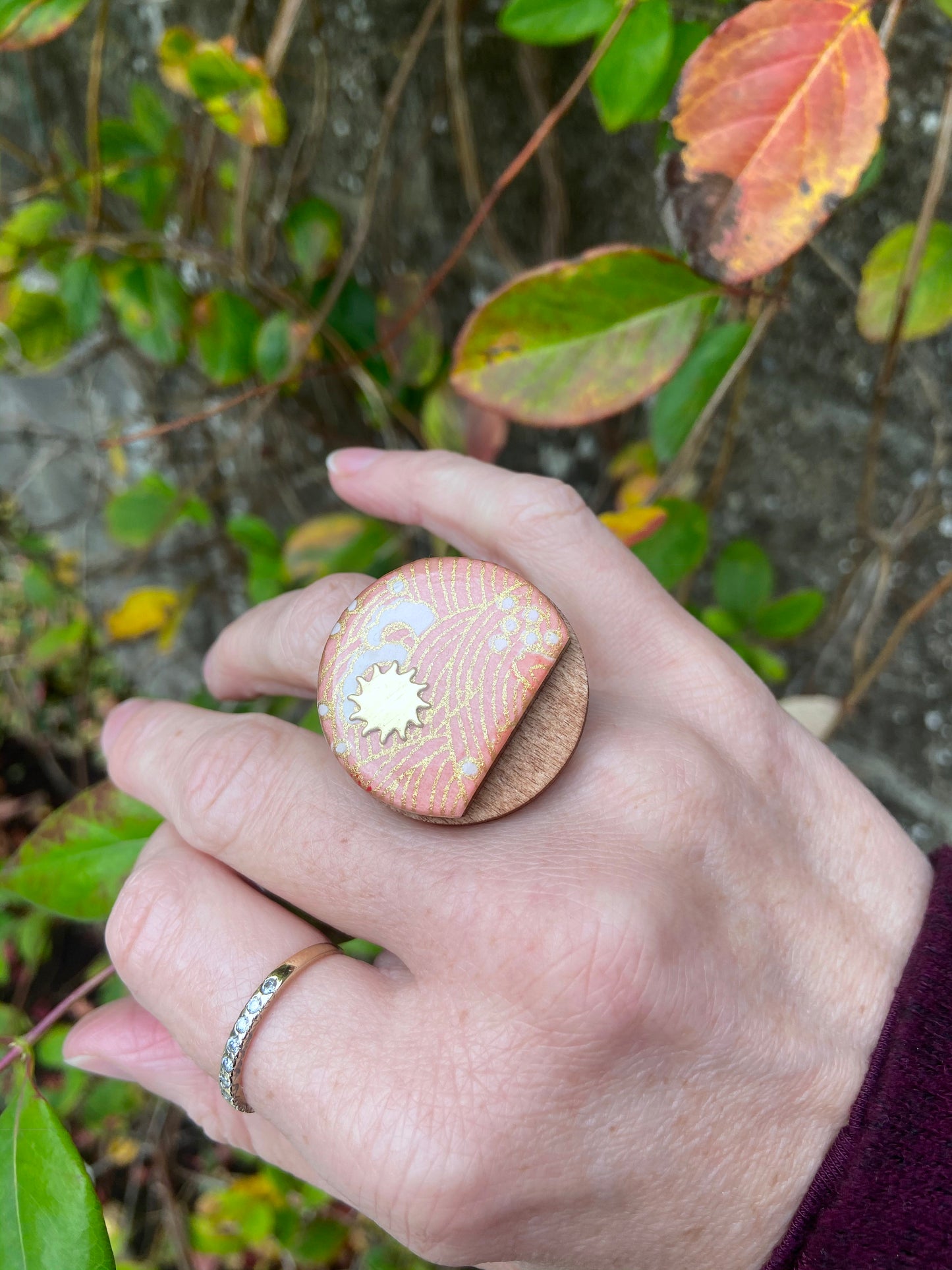 Hand wearing a large wooden ring with a gold center against a natural background