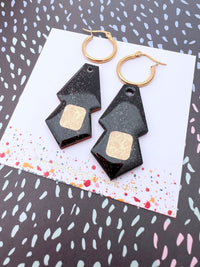 Black geometric earrings with gold accents on a patterned card