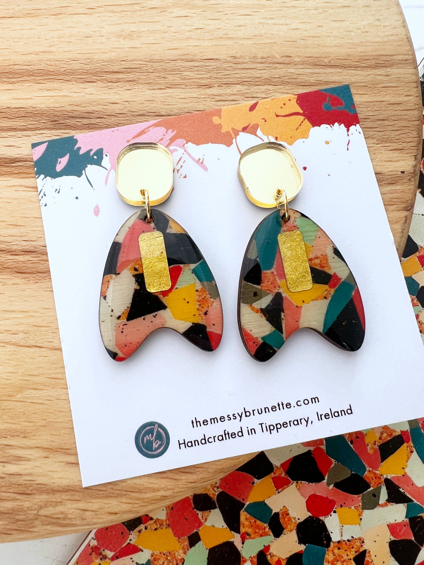 Colourful mosaic style earrings on a branded card with 'themessybrunette.com' on a wooden surface.