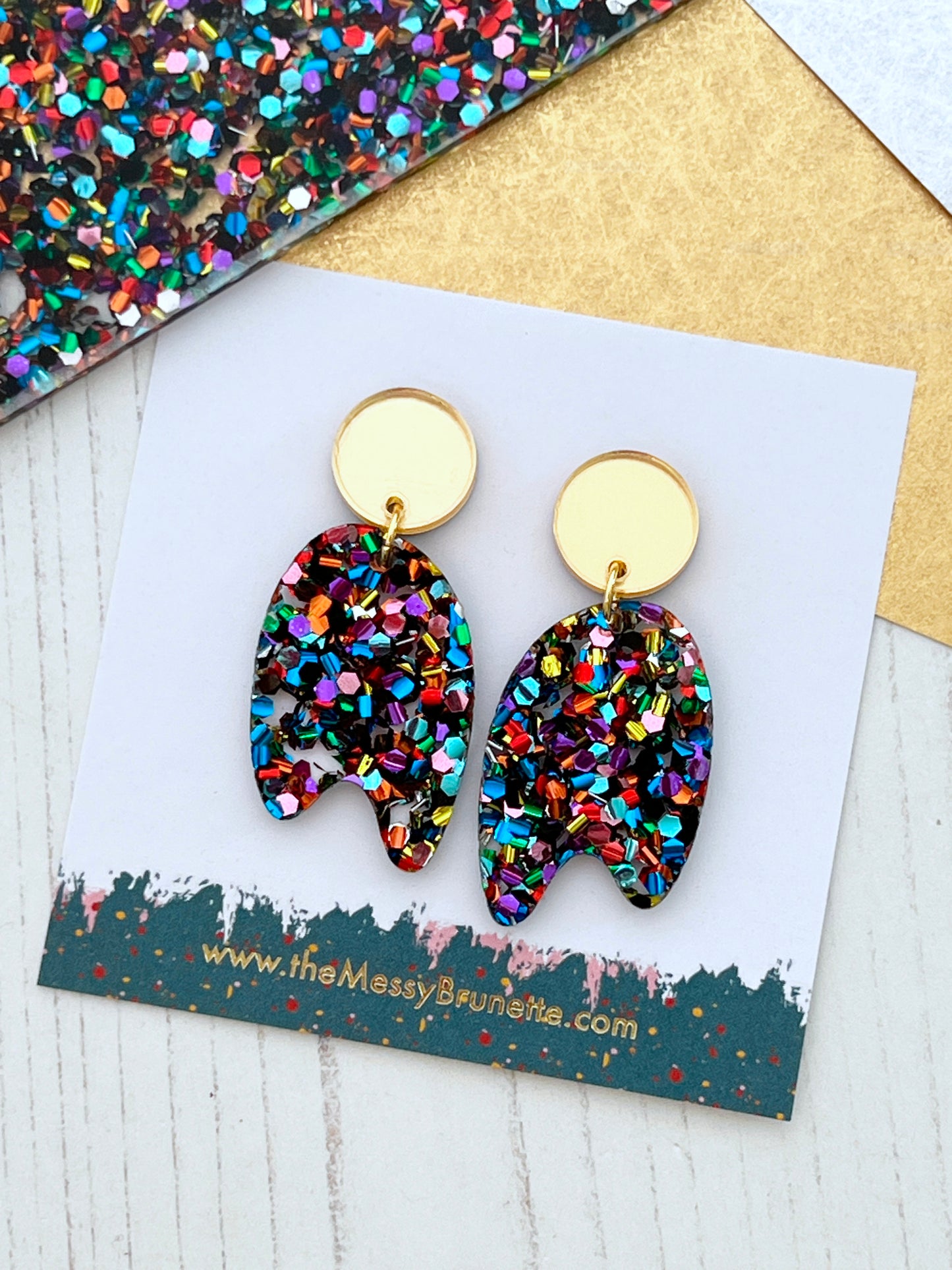 Multicoloured confetti glitter earrings on a branded card with a glittery background