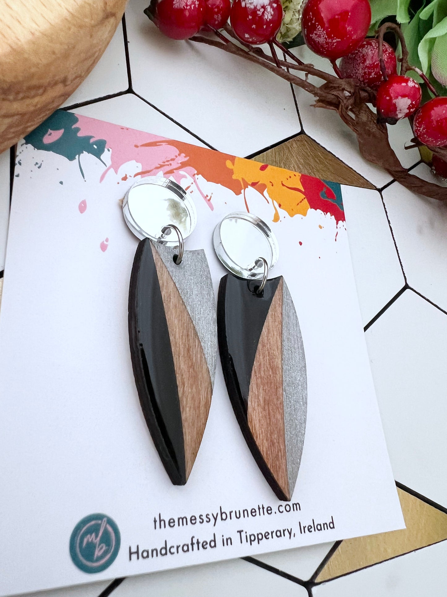 Pair of black and silver wood earrings on a branded card with decorative background