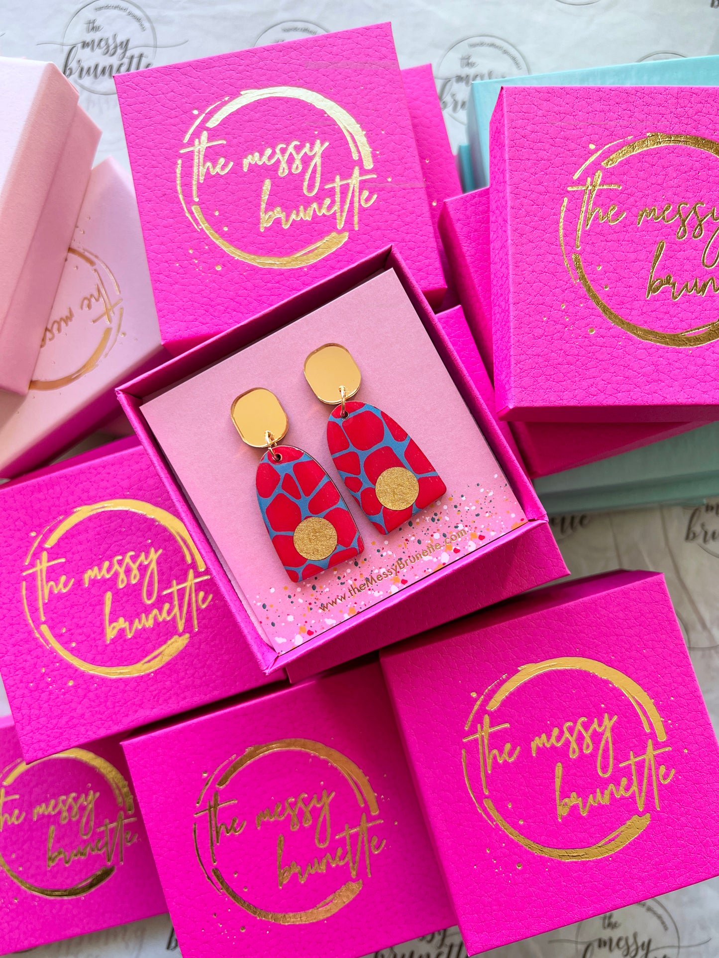 red and blue safari print wooden earrings surrouded by the The Messy Brunette jewellery branded boxes