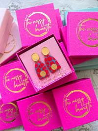 red and blue safari print wooden earrings surrouded by the The Messy Brunette jewellery branded boxes