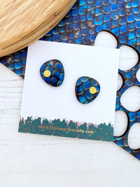 Blue and gold earrings on a branded card with seashells and wood in the background