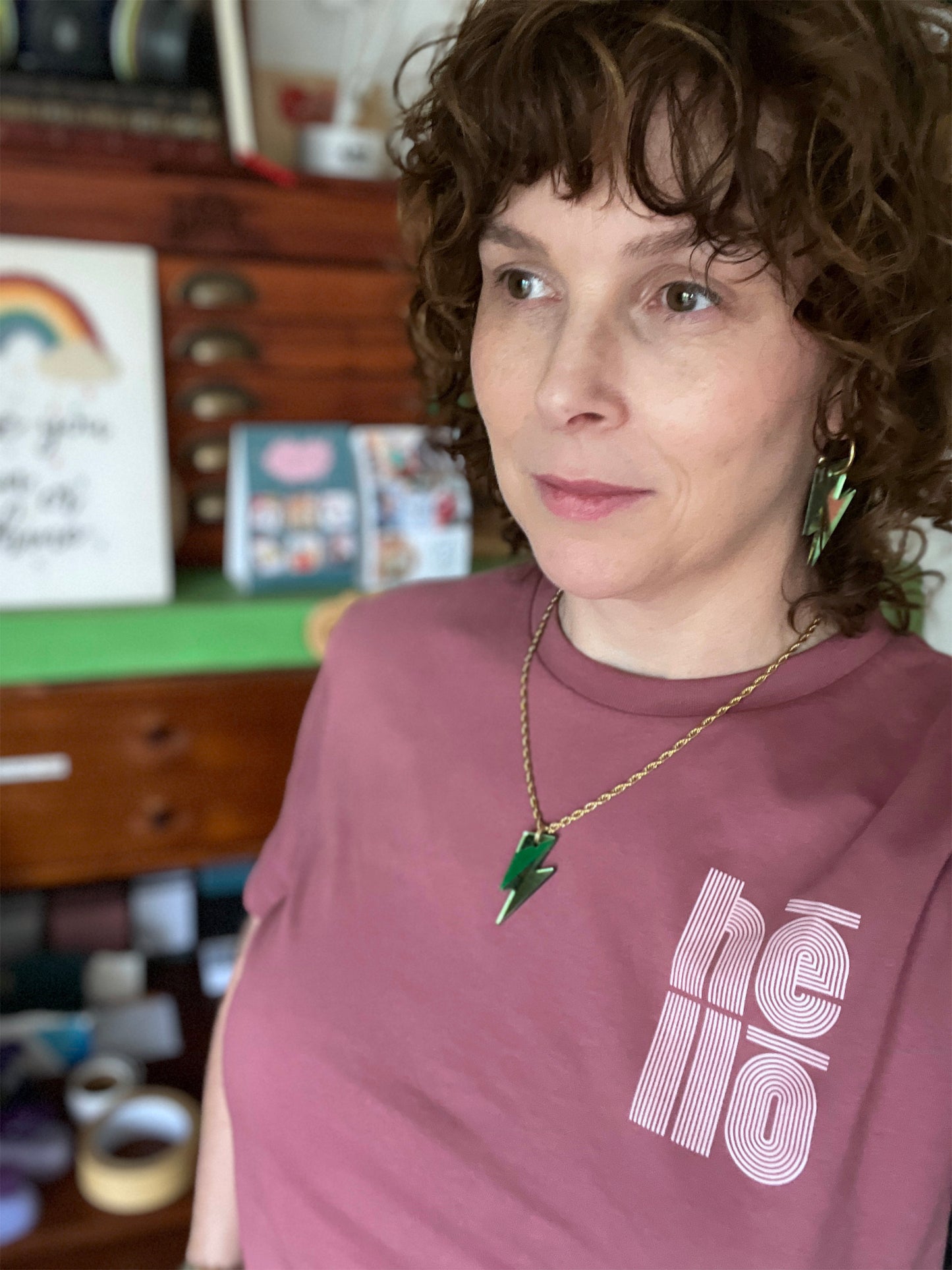Person wearing a green bolt necklace ,standing in a room with shelves and books.