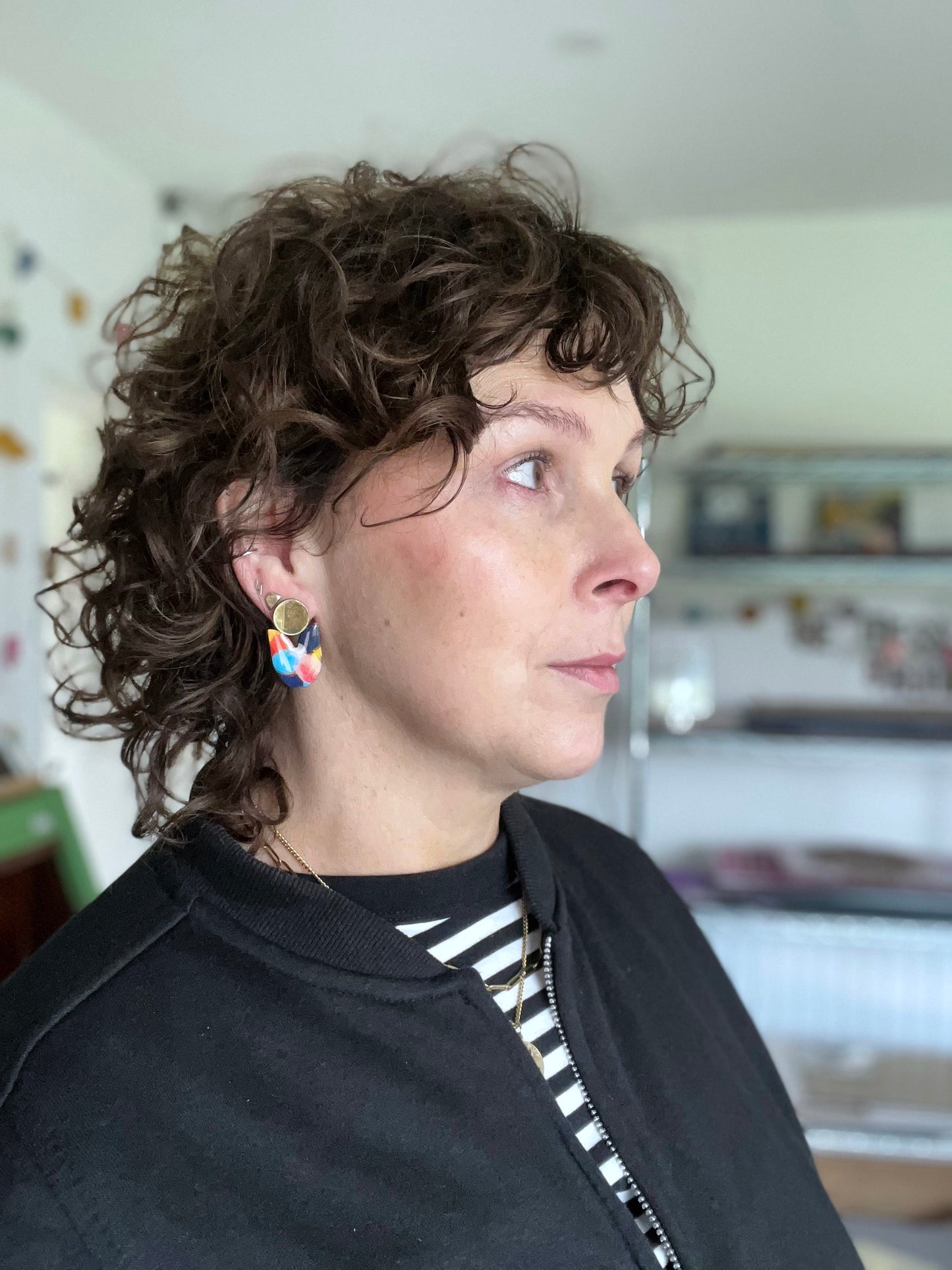 Person with curly hair wearing colourful earrings indoors
