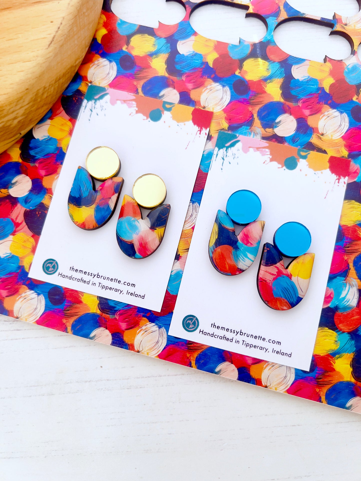 Colouful multi colour painted wood earrings on branded cards with a colourful patterned background