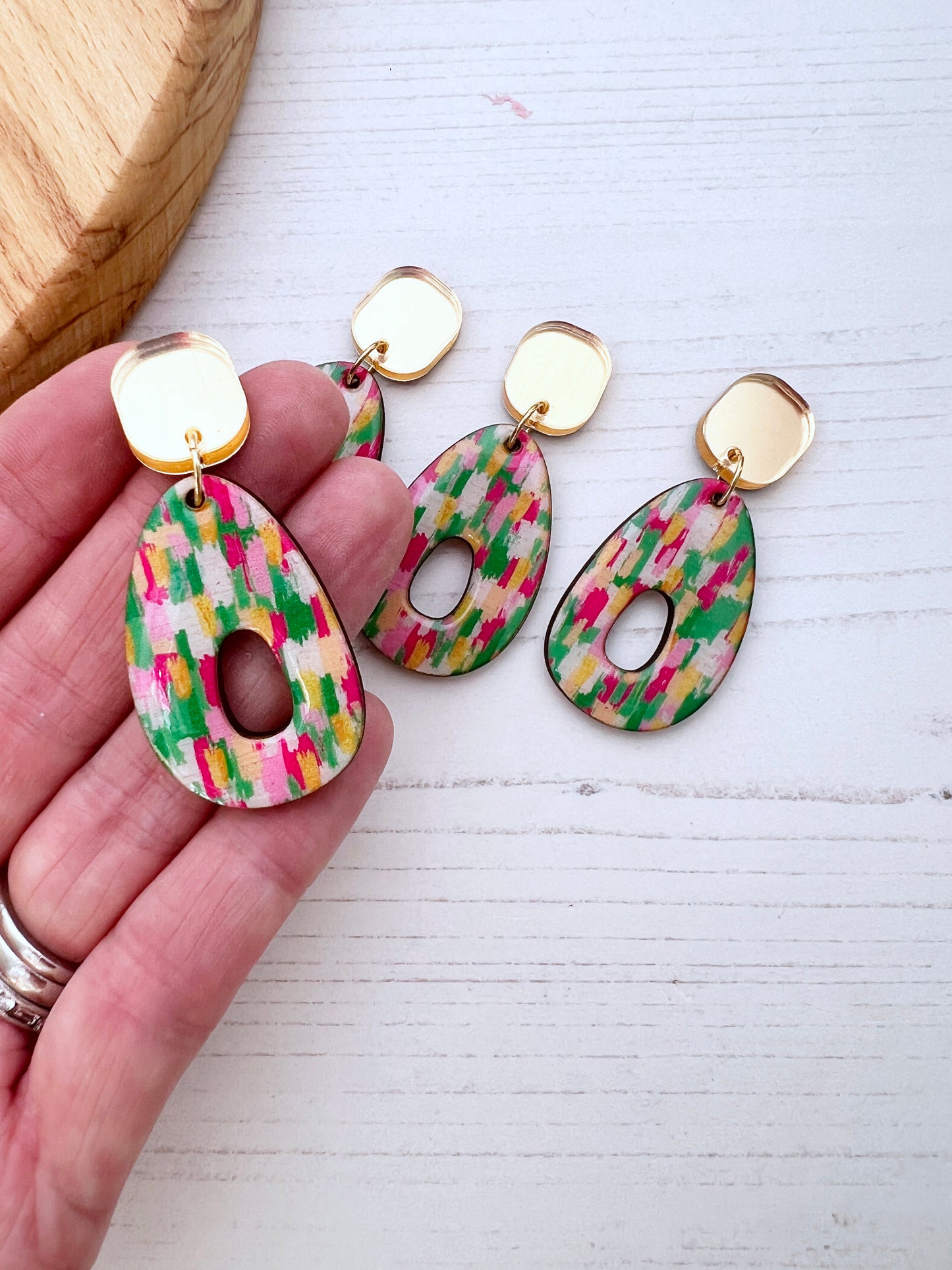 Colourful patterned earrings held by a hand on a white surface