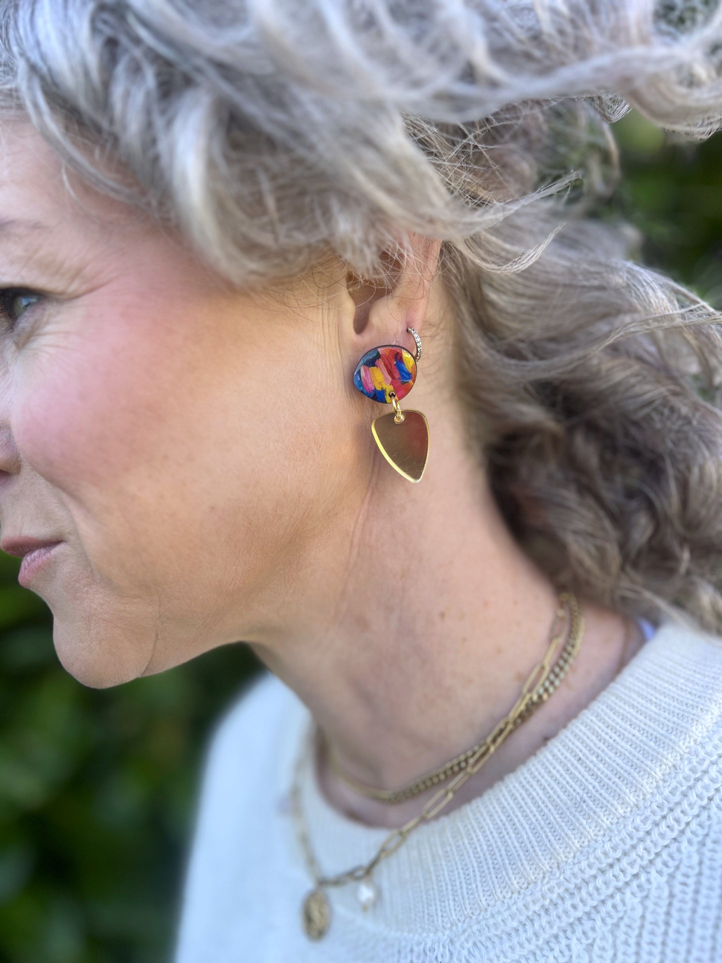 Close-up of a person wearing colourful earrings with a blurred natural background