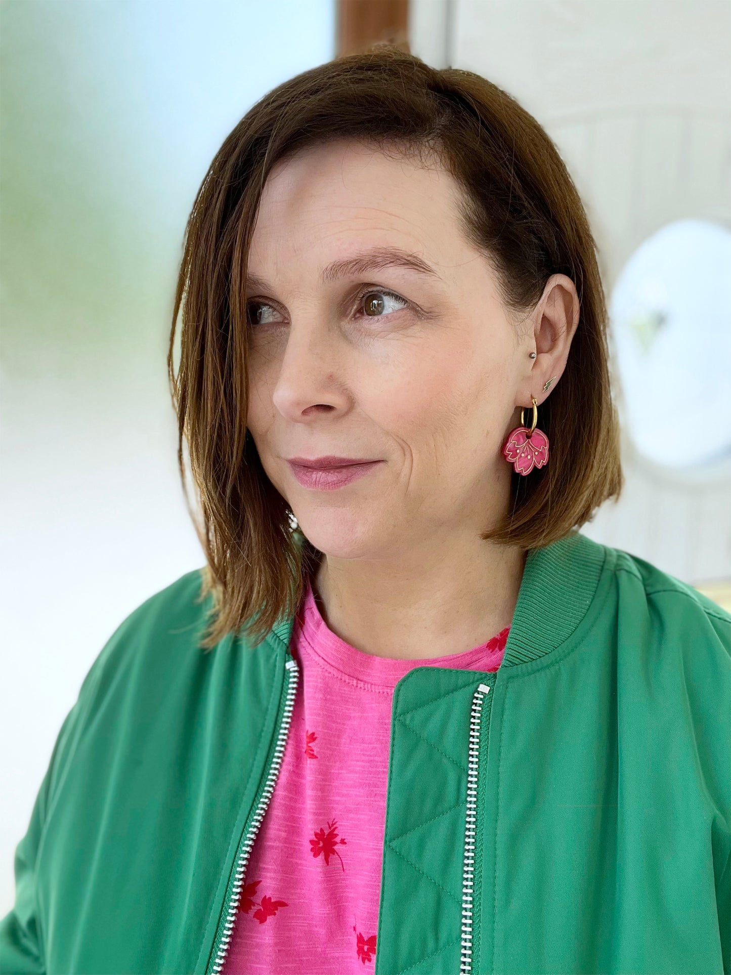 Woman wearing a green jacket and pink shirt with cherry blossom hoop earrings indoors