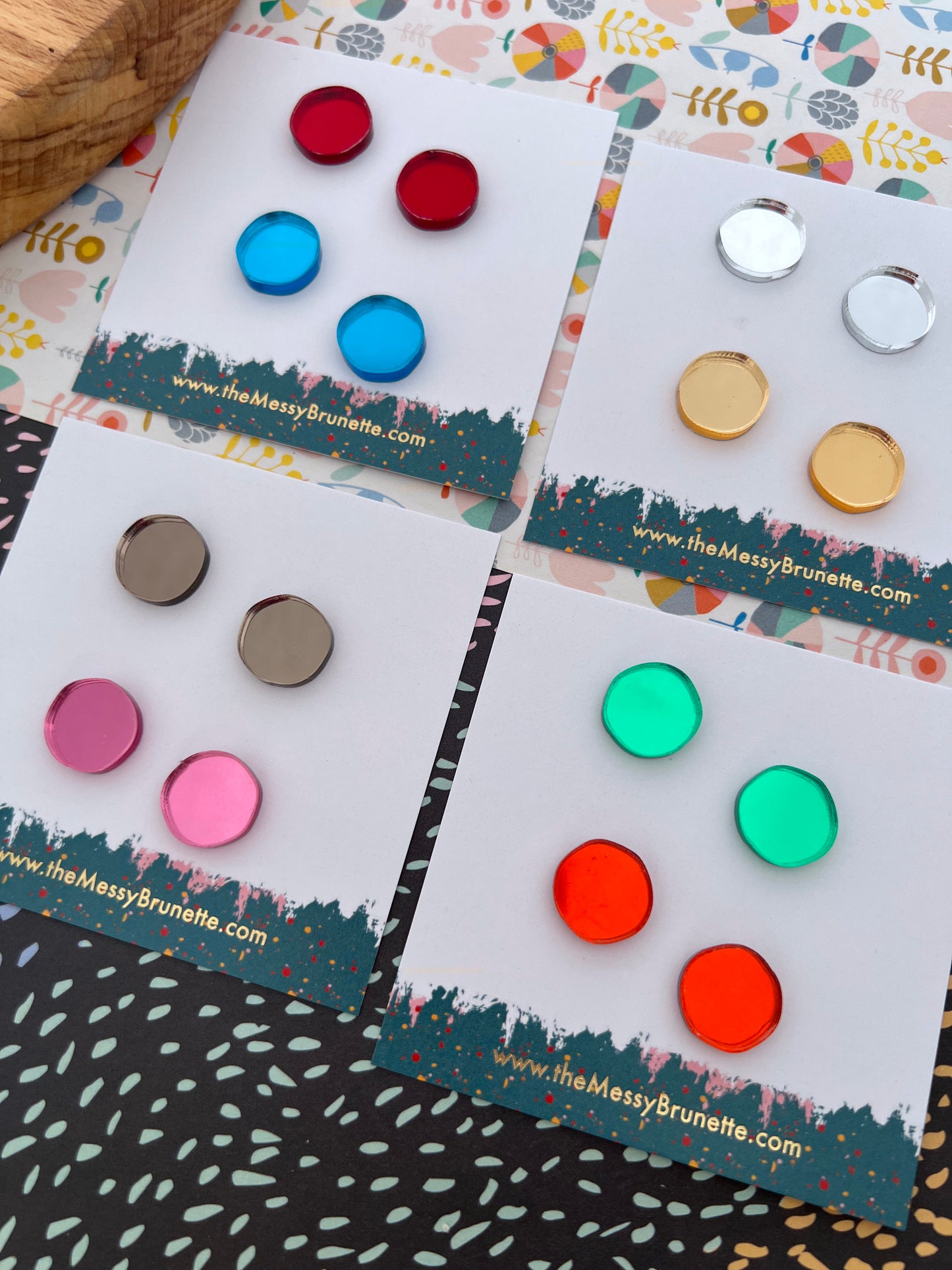 Colourful acrylic stud earrings on display with branded cards on a patterned surface