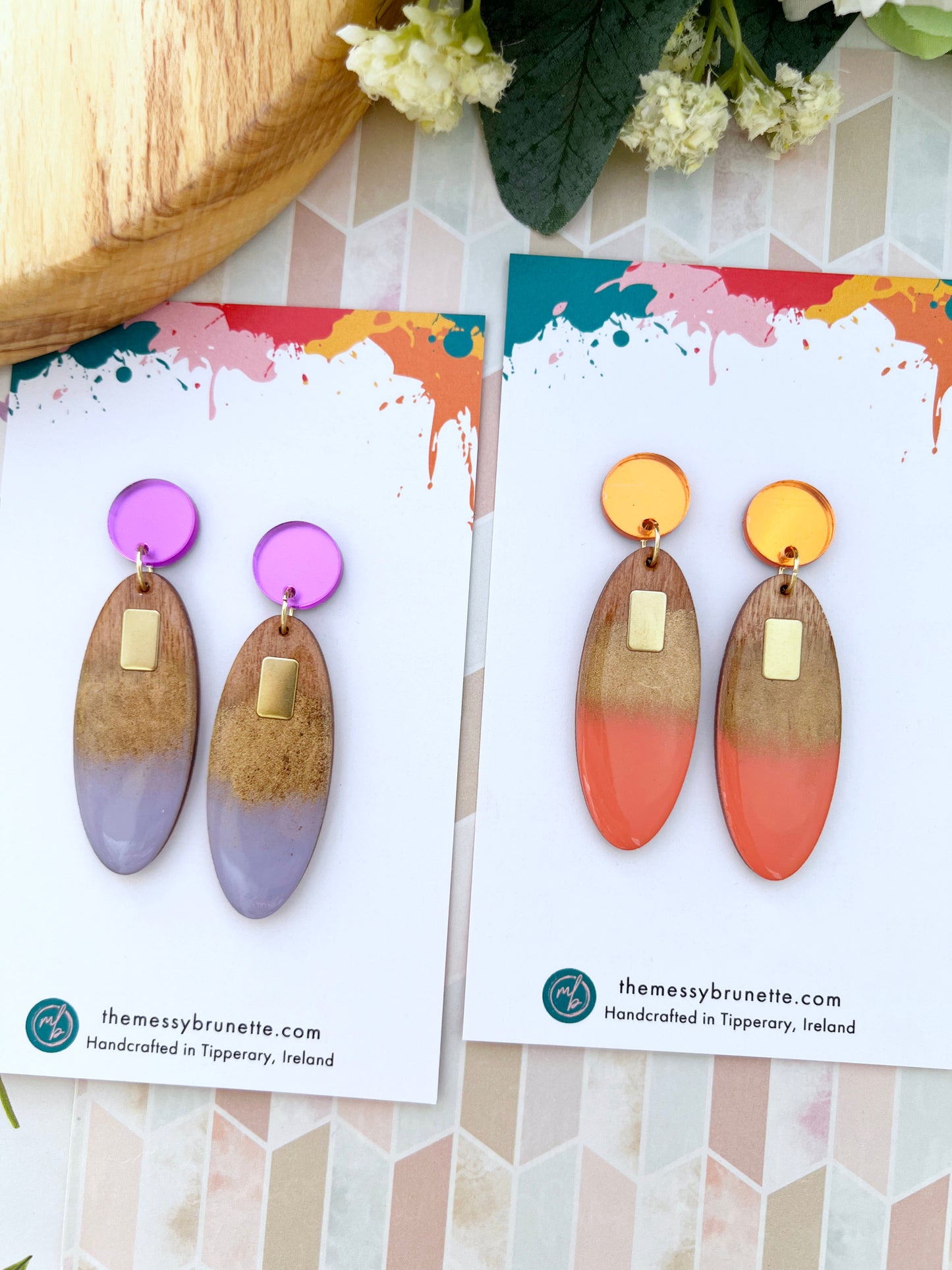 Pair of painted oval wood earrings on a branded card with a colourful background
