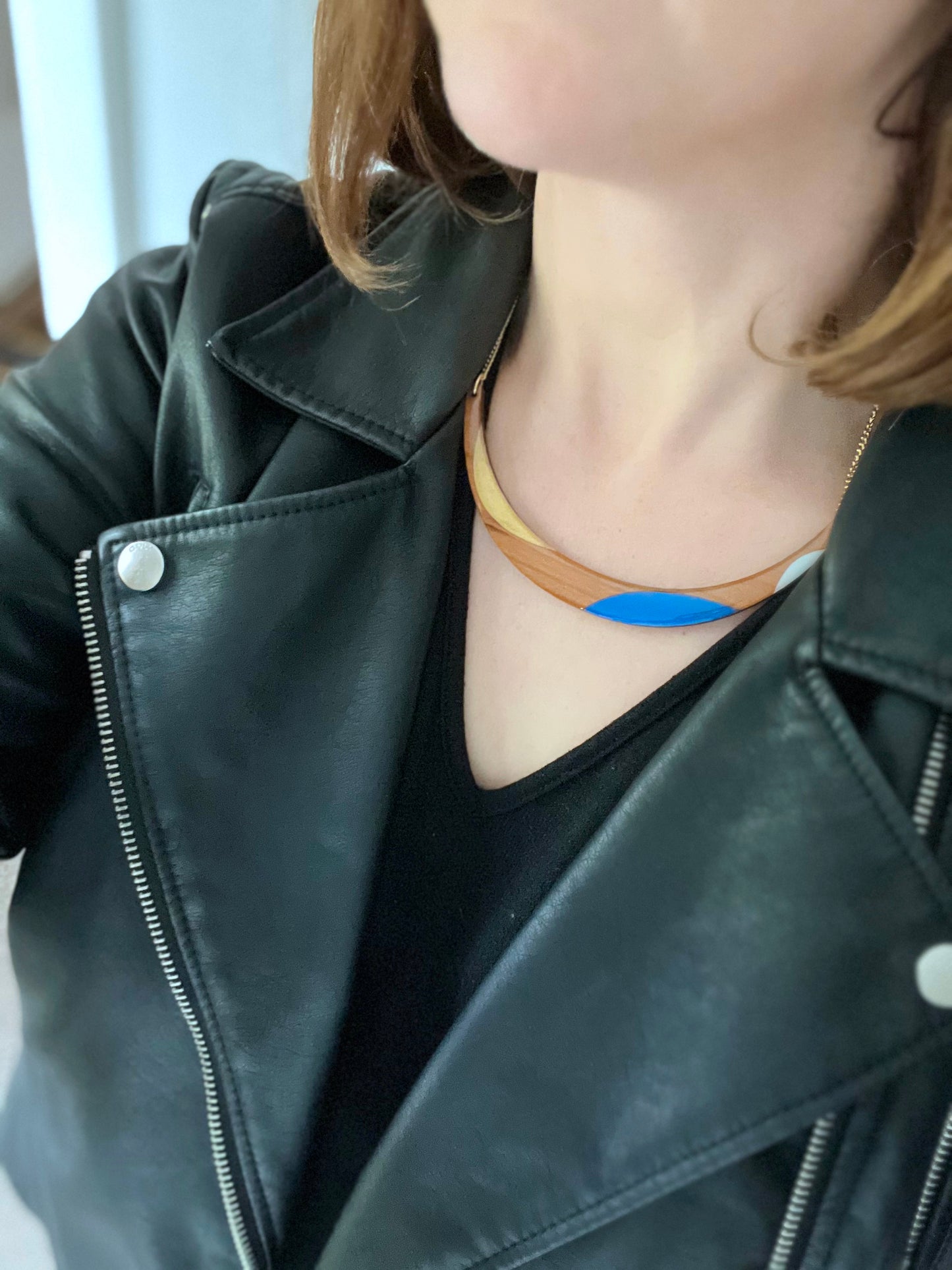 Person wearing a black leather jacket with a blue and gold wood necklace 