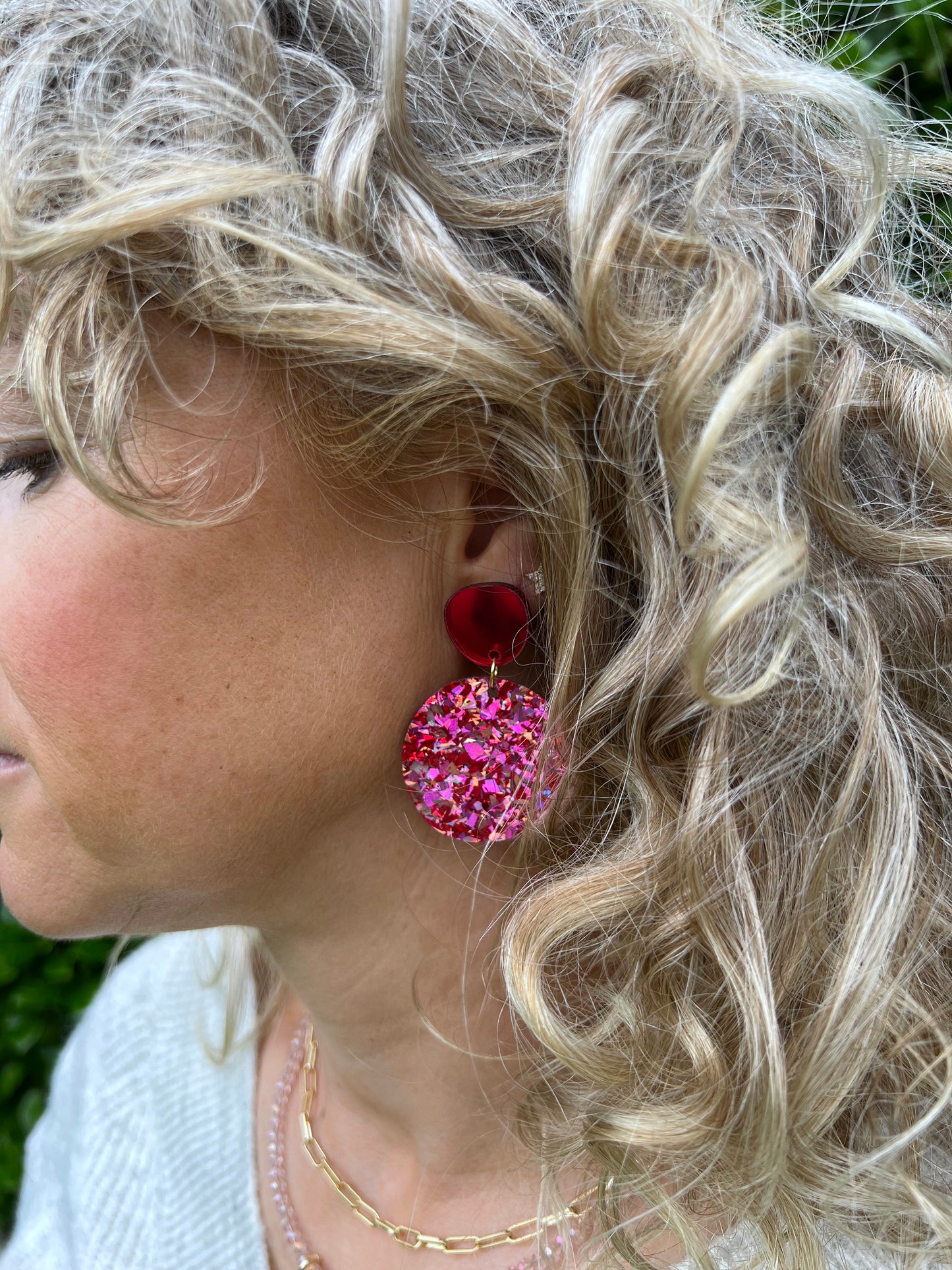 Close-up of a person wearing pink and red glittery disco dot earrings with a blurred background