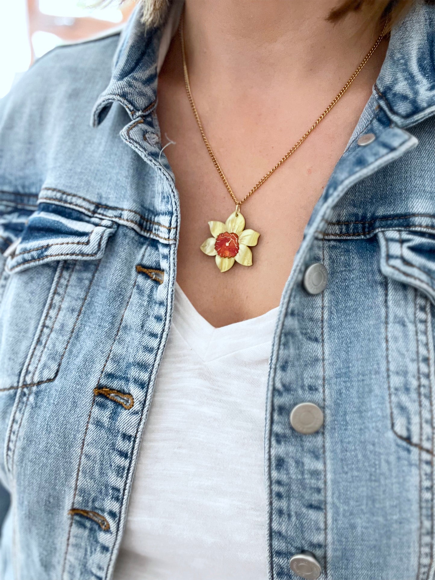 Person wearing a denim jacket with a necklace featuring a daffodill pendant.