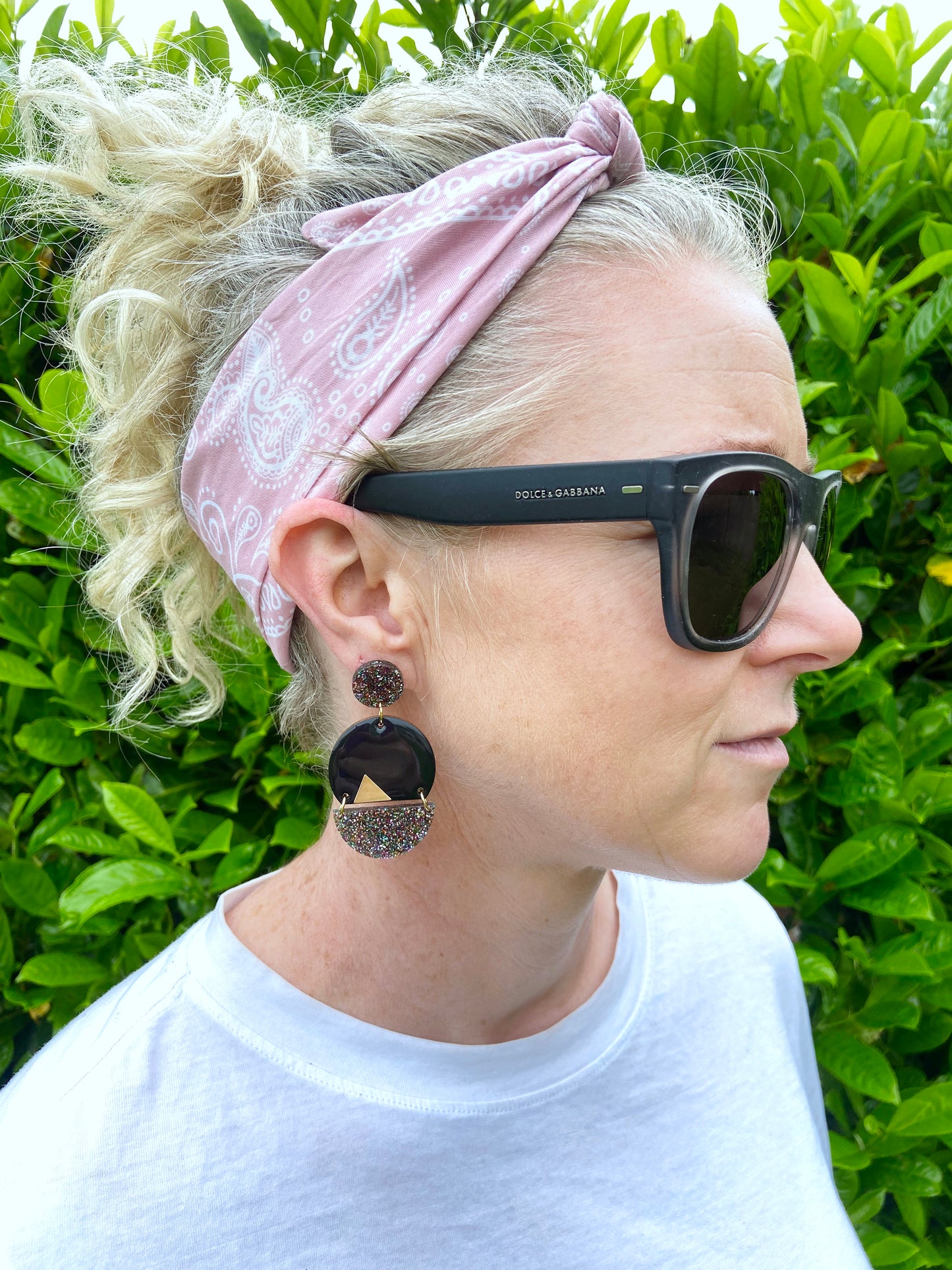 Person with a pink headband and sunglasses wearing black glitter earrings