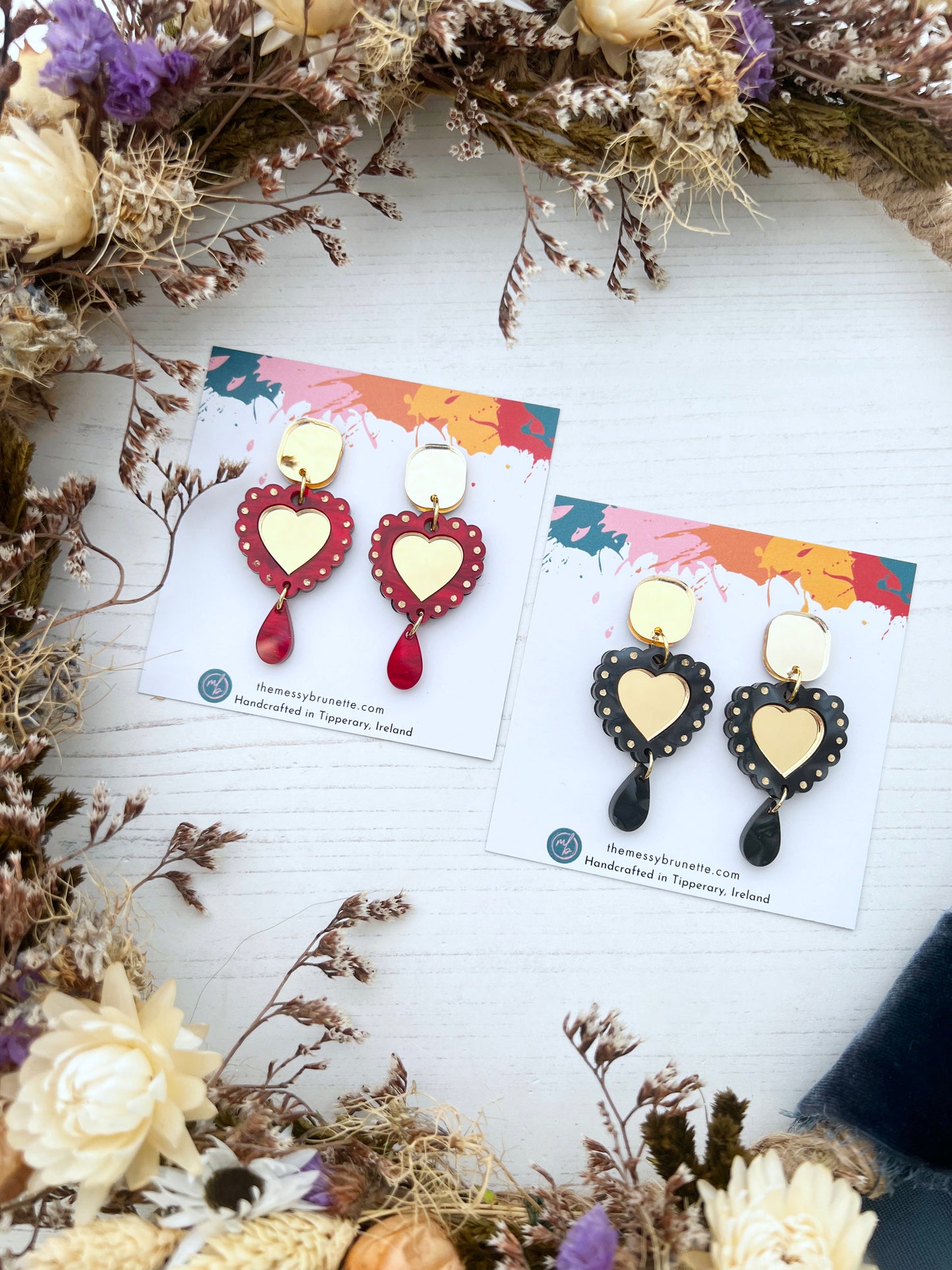 Heart-shaped earrings on display cards with dried flowers around