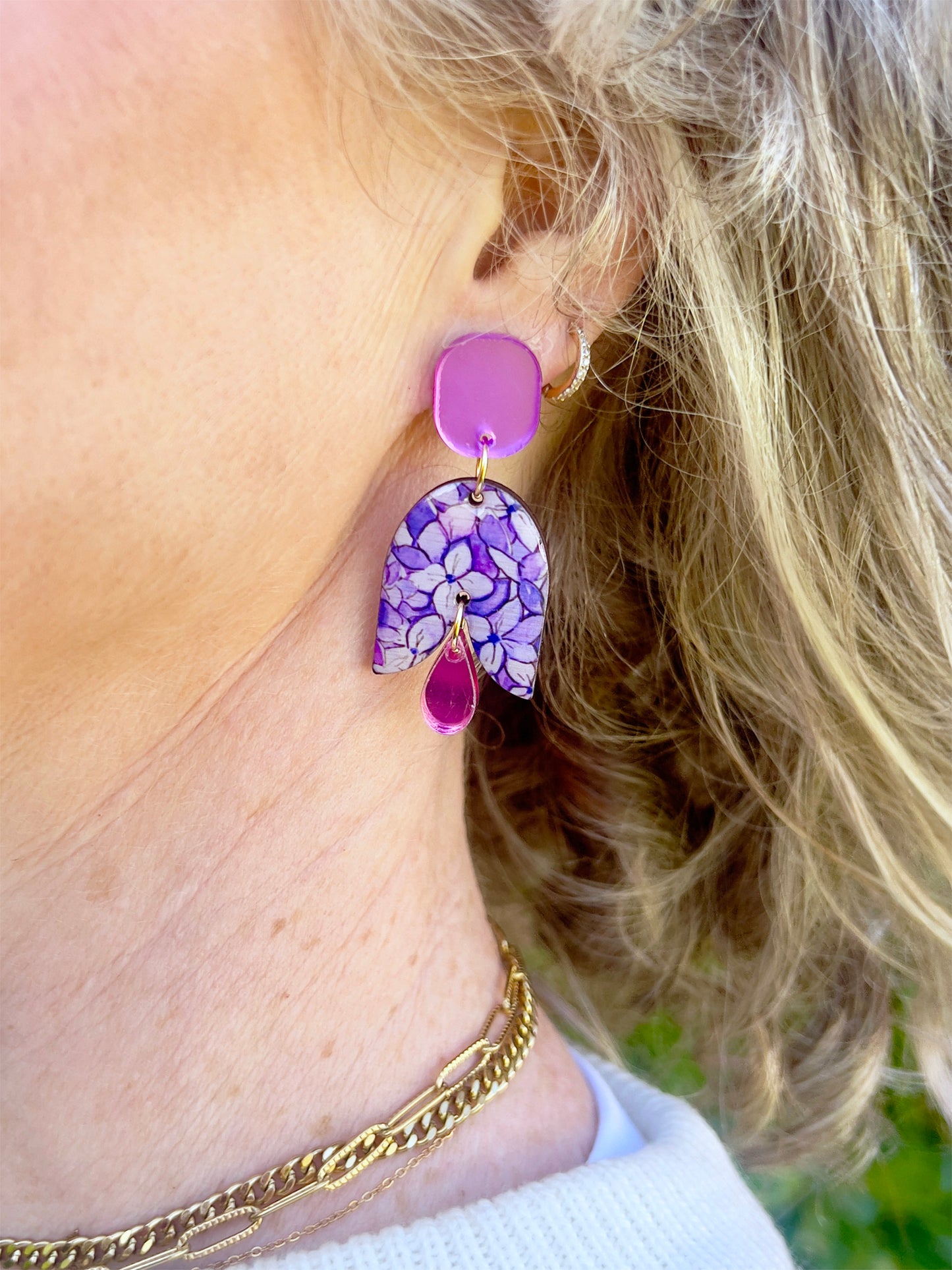 Close-up of a person wearing a purple floral earring with a pink accent.