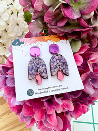 Pair of hydragea floral-patterned earrings on a card with 'themessybrunette' branding, displayed among pink flowers.