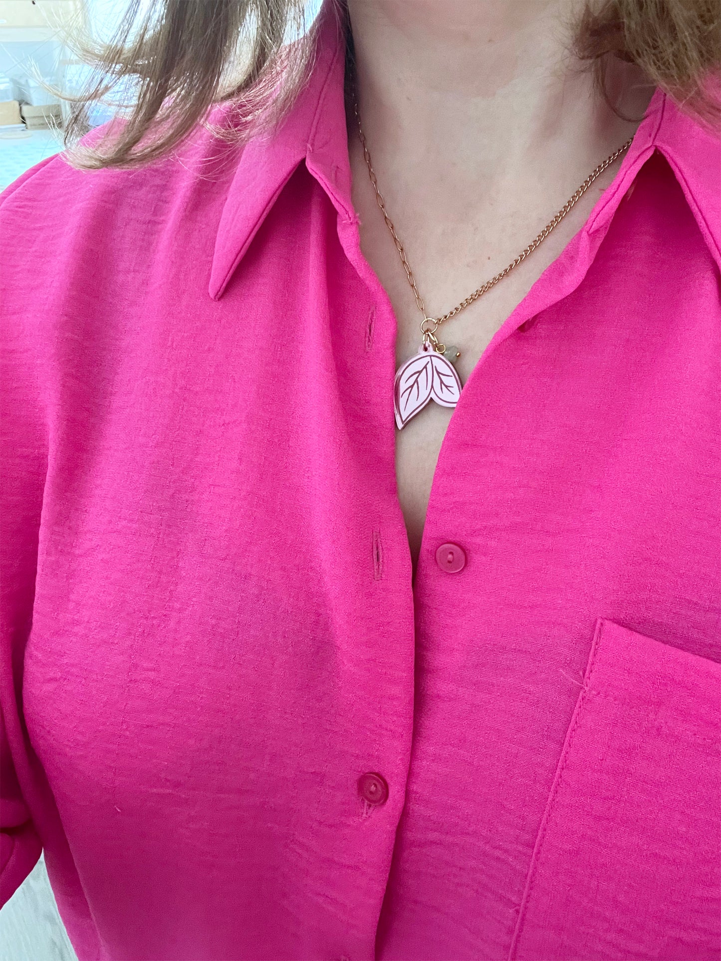 Person wearing a bright pink shirt with a necklace featuring a leaf pendant.