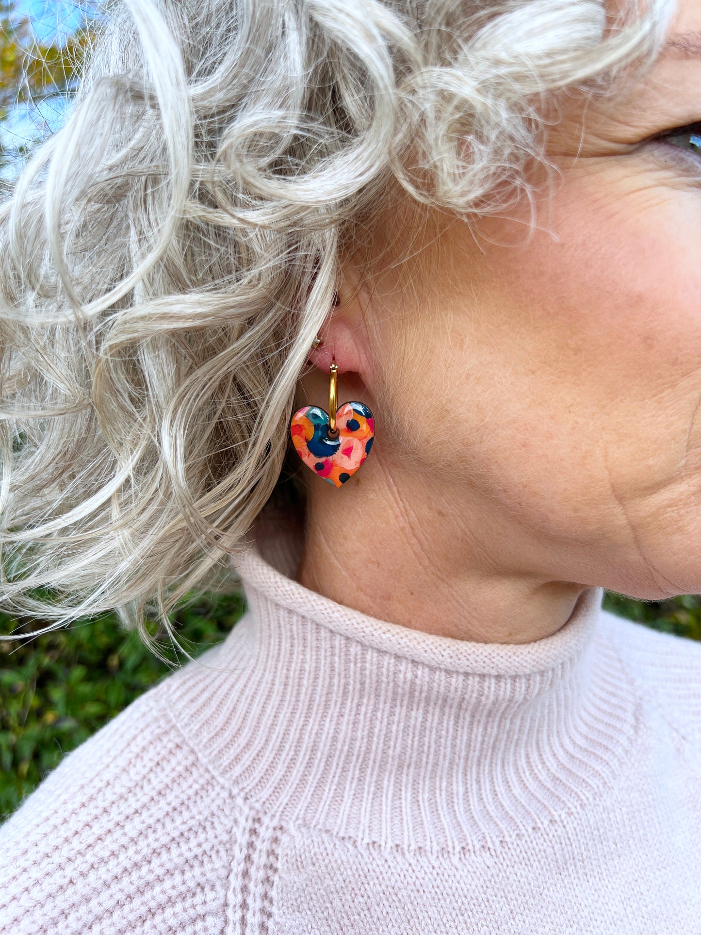 Person wearing colorful mini blossom heart shapred earrings on hoops