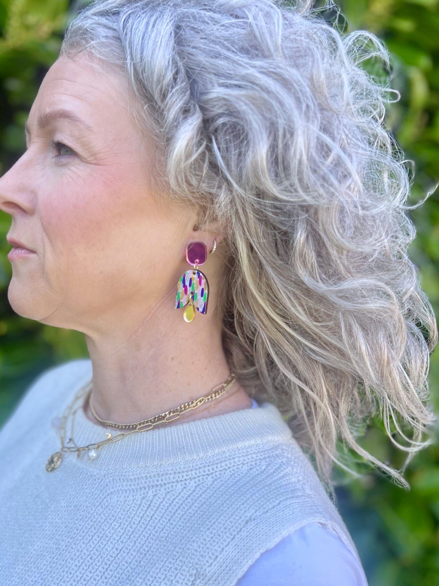 Woman with curly gray hair wearing colourful earrings against a green background