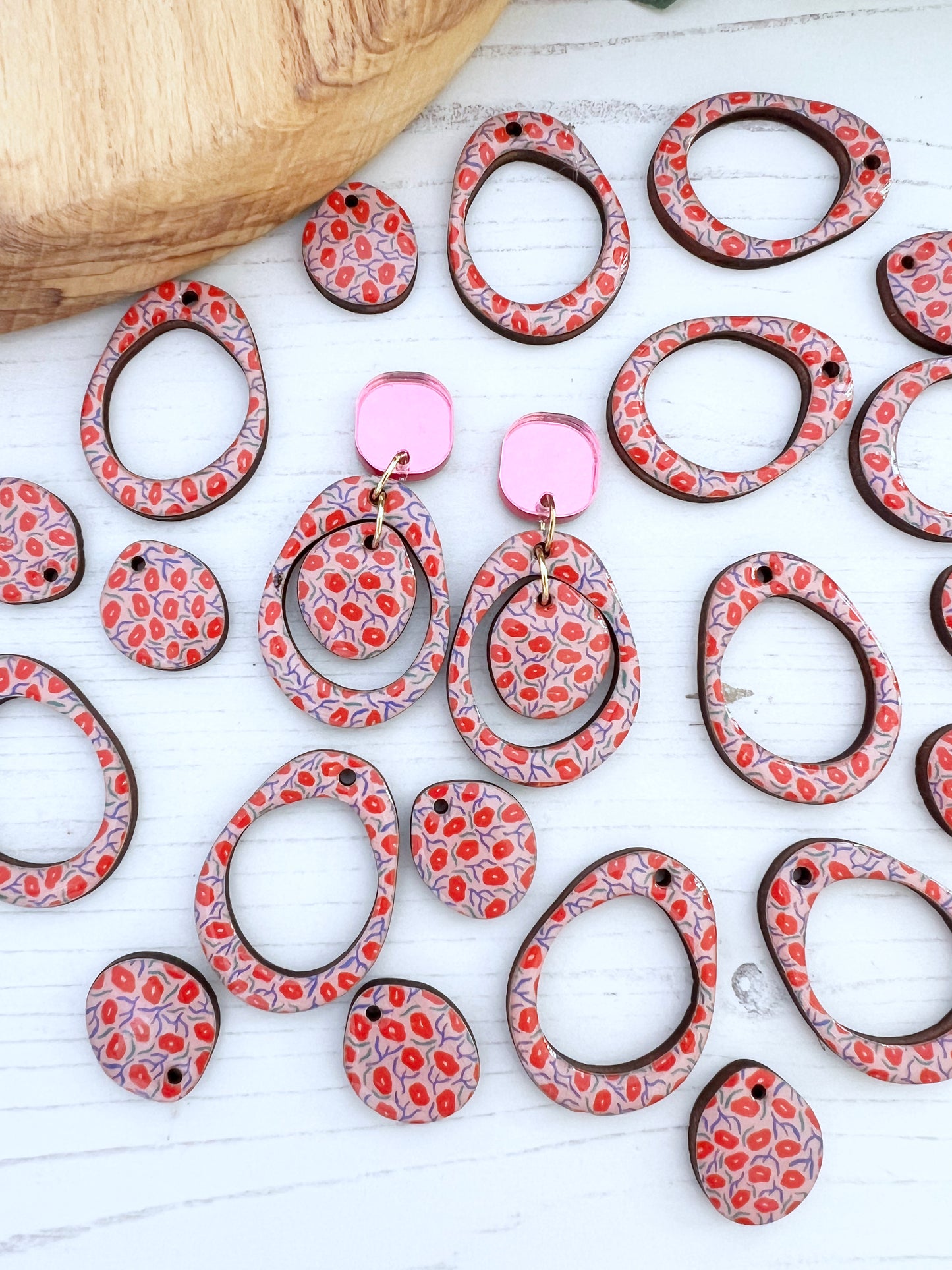 Decorative earrings with red and white pattern on a light wooden surface