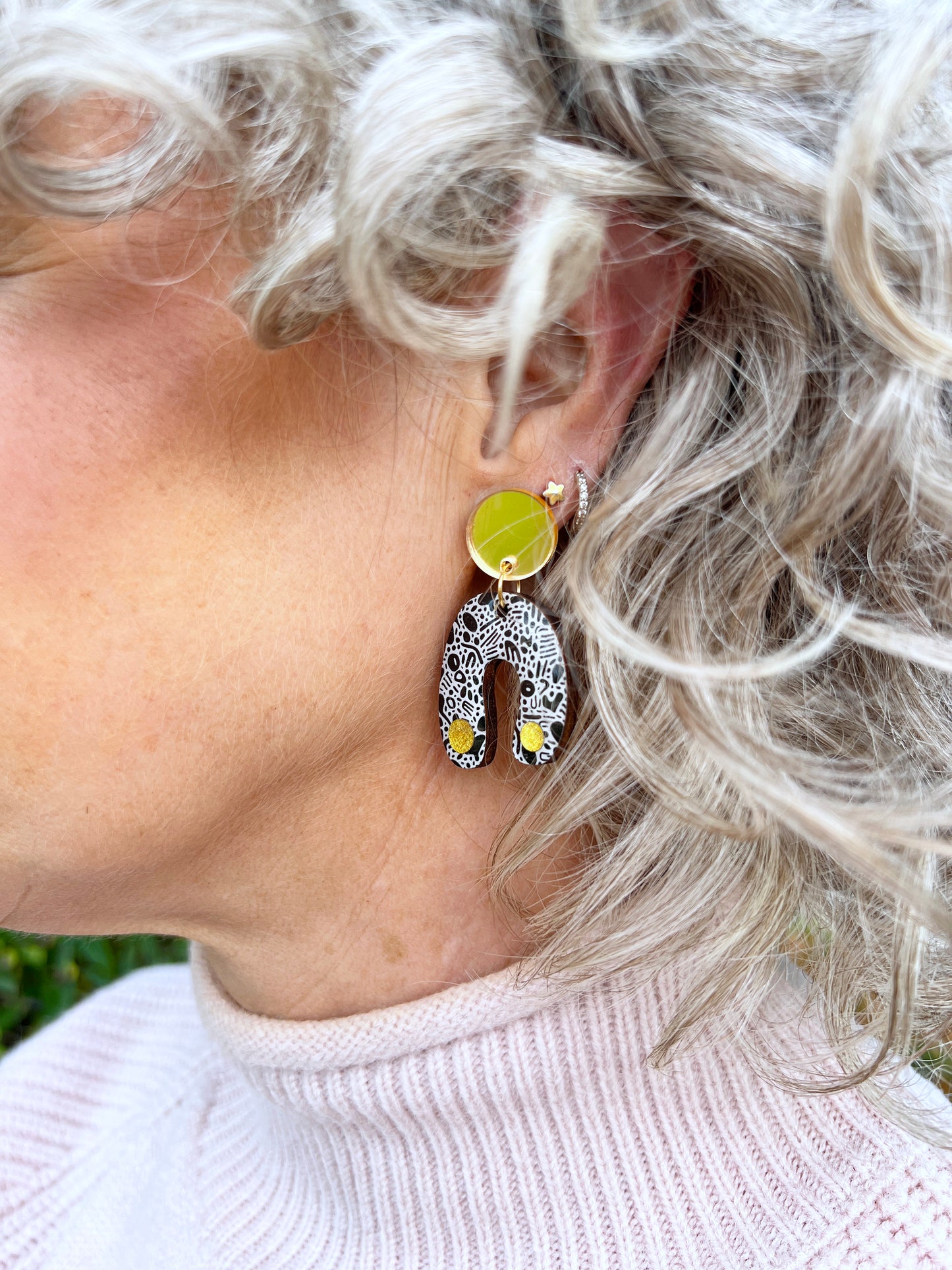 Close-up of a person wearing a monochrome earrings in an arch shape with gold studs