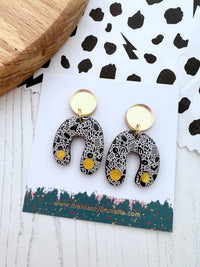 Pair of monochrome arch earrings on a branded card with a polka dot background