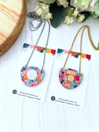 Colourful necklace with mosaic pattern on a white surface with flowers in the background
