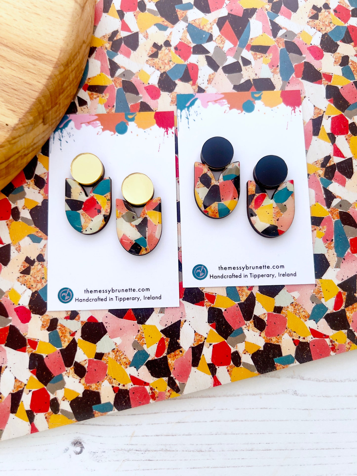 Colourful earrings on branded cards with a multicolored patterned surface.