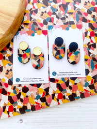 Colourful earrings on branded cards with a multicolored patterned surface.