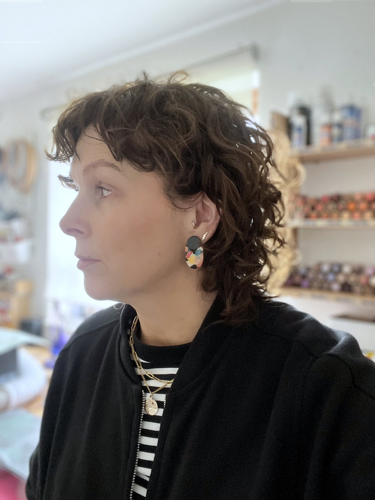 Person wearing colourful earrings in a blurred indoor setting