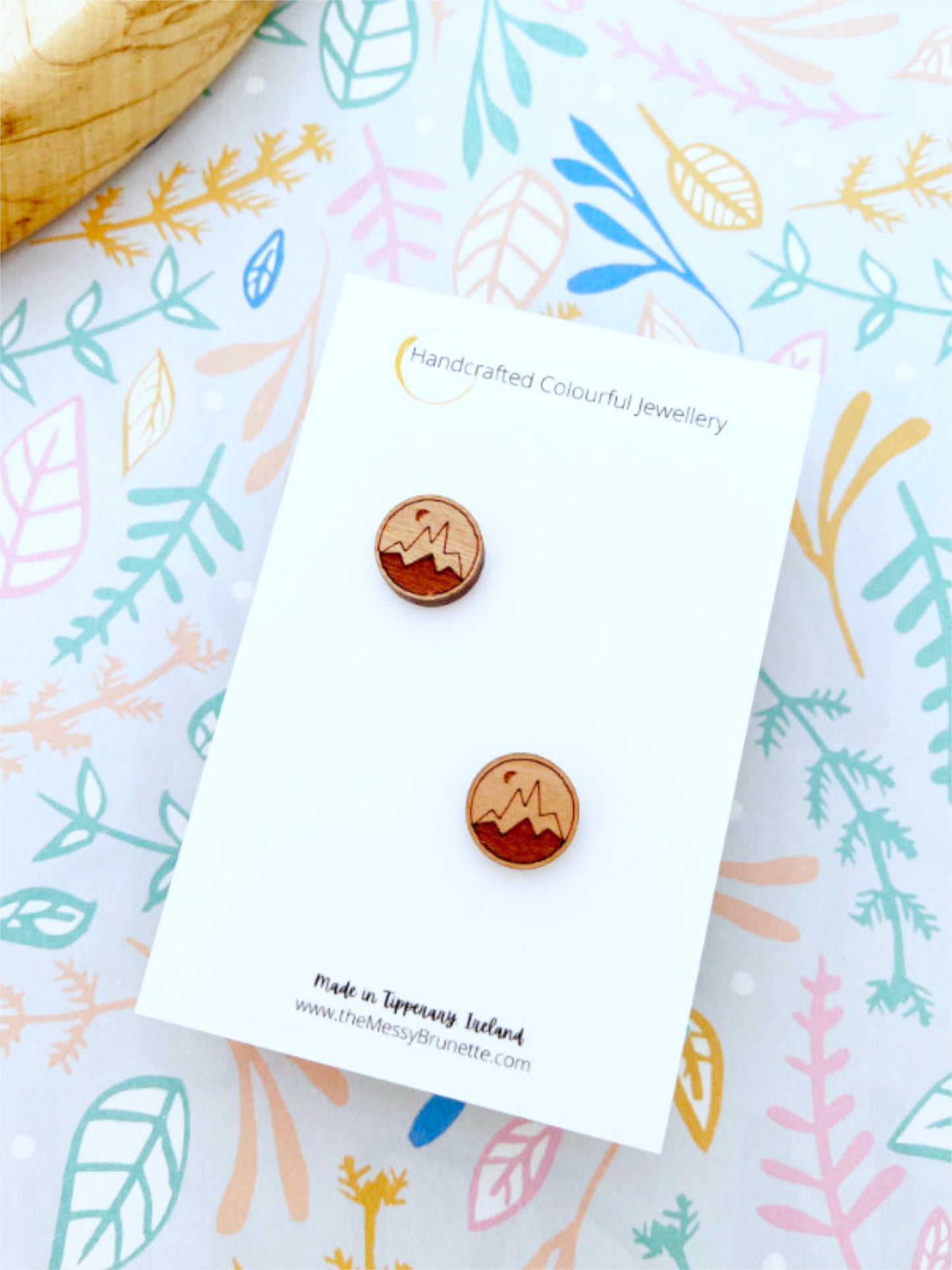 Wooden earrings on a card with a colorful leaf patterned background