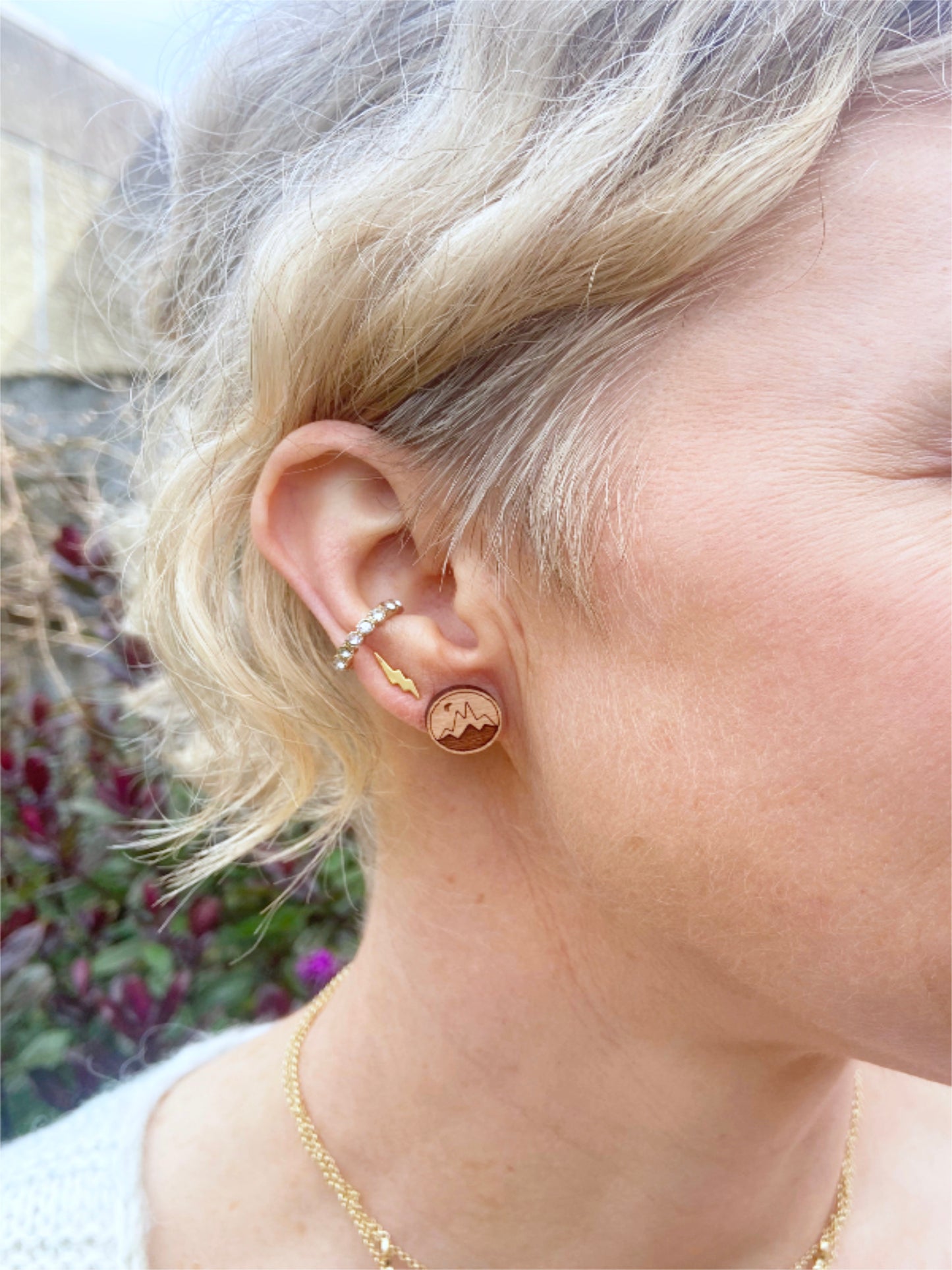 Close-up of a person wearing small wodden stud earrings with a blurred outdoor background