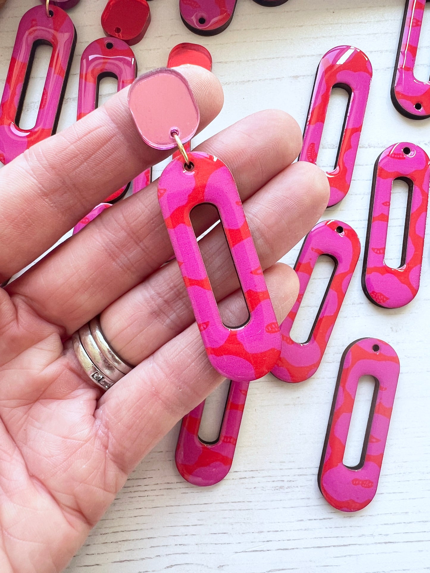 Pink and red patterned earrings held in a hand with a light background