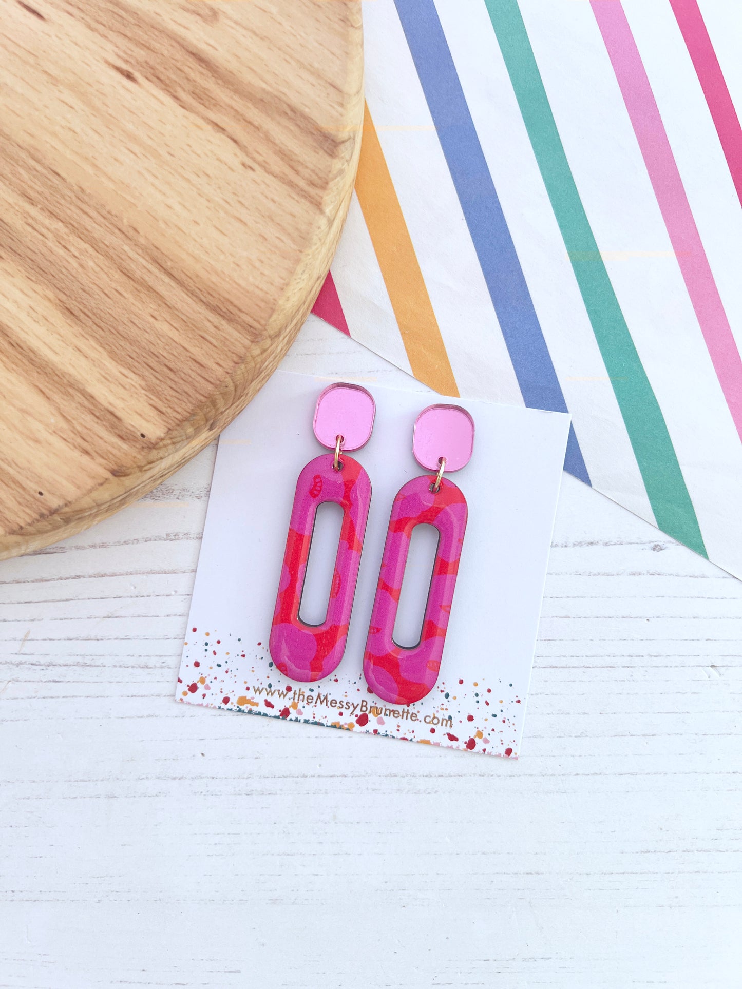 Pink and red abstract earrings on a white card with colourful striped background