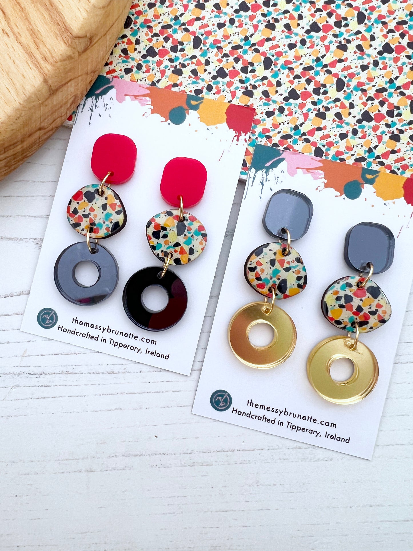 Colourful earrings on branded cards with a patterned background